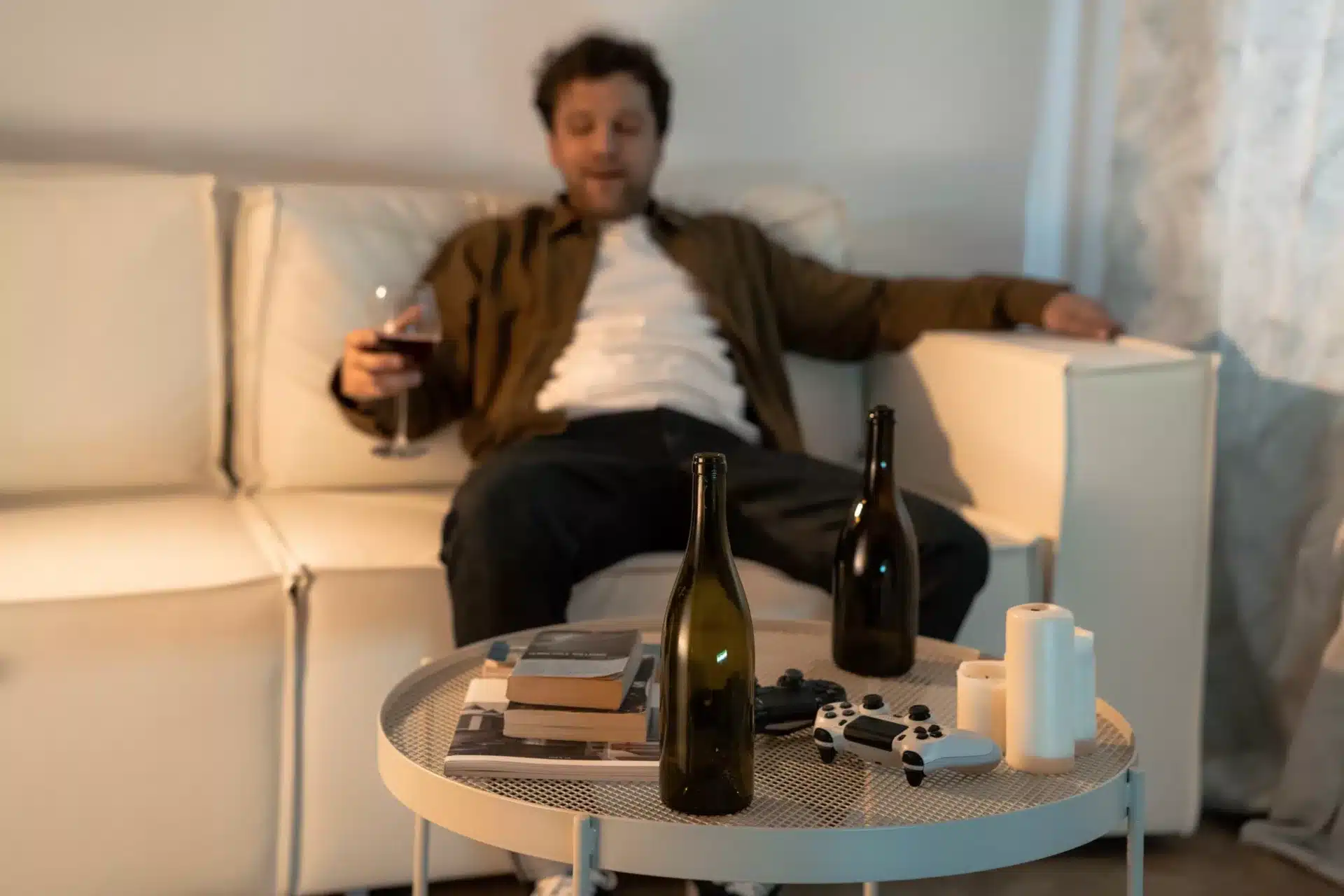 Man Sitting on White Sofa with Glass of Wine Beside Table with Bottles and Candles