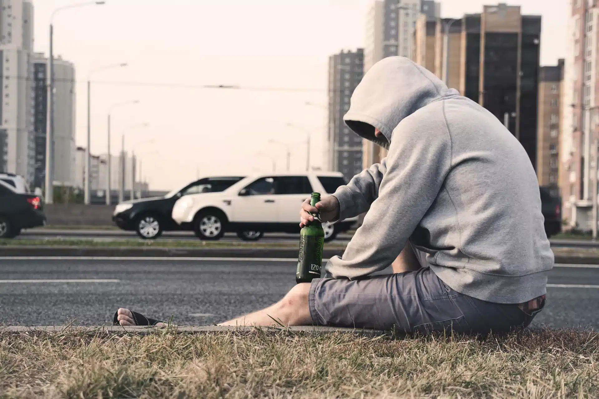 Person in Gray Hoodie Holding Beer at the side of the road