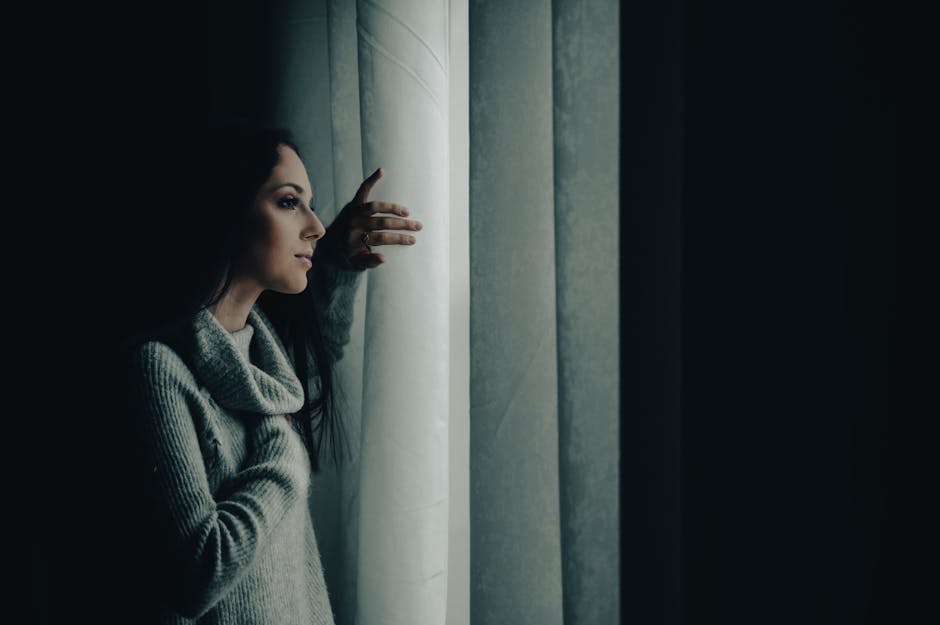person looking thoughtfully out a window with a faint shadow - Post-acute withdrawal syndrome